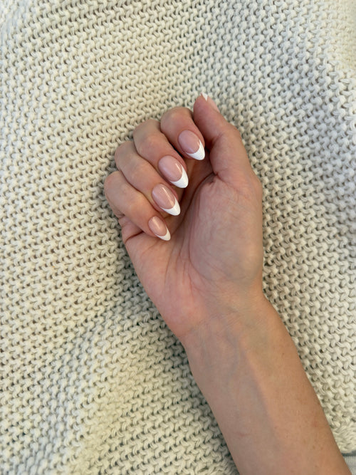 Blush press-on nails worn on hand resting on cream knit — nude base with white French almond tips